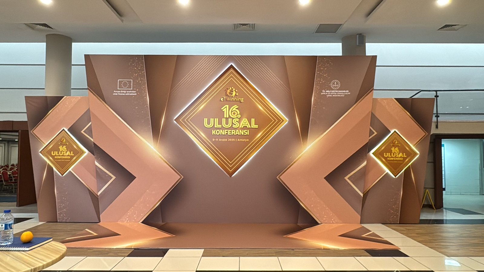 Antalya'da 16. Ulusal Konferans için kurulmuş, bakır renkli, elmas desenli ışıklı konferans sahne podyumu ve dekoru.