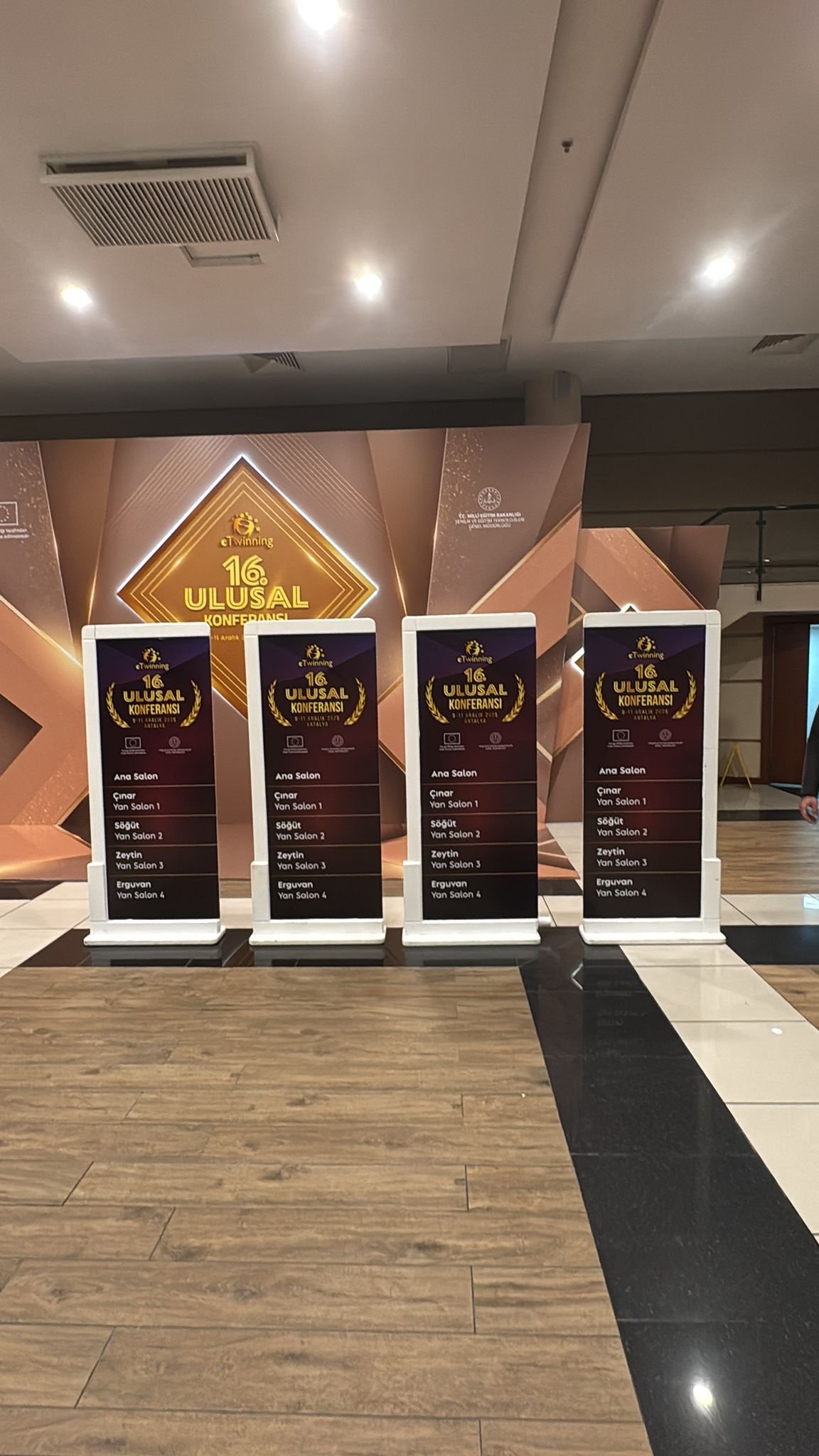 Siyah ve gold renkli, 16. Ulusal Konferans için hazırlanmış ayaklı konferans yönlendirme panosu ve salon listesi tabelaları.